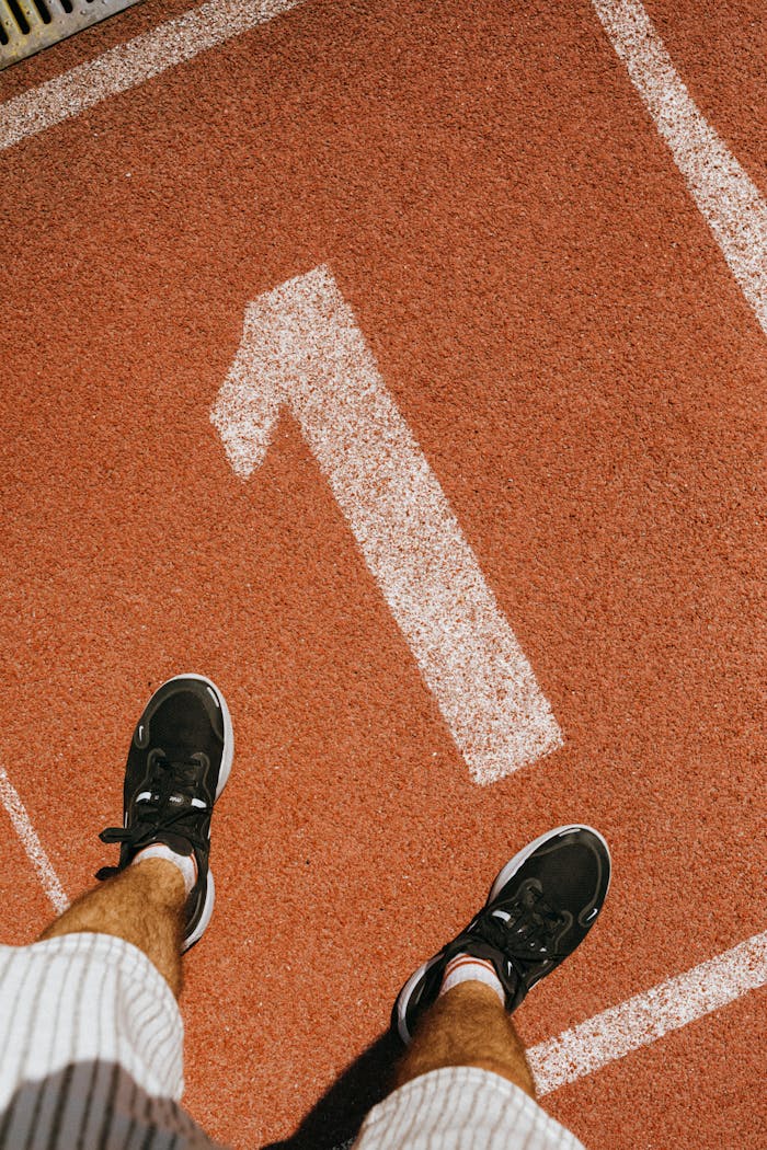 heros-img Man standing on number one lane of outdoor running track wearing sports shoes.
